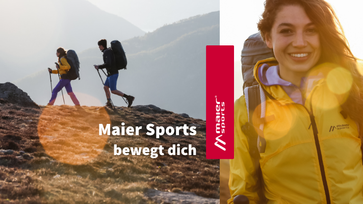 Zwei Personen wandern mit Wanderausrüstung. Rechts im Bild zu sehen ist eine Frau, die eine gelbe Jacke trägt.