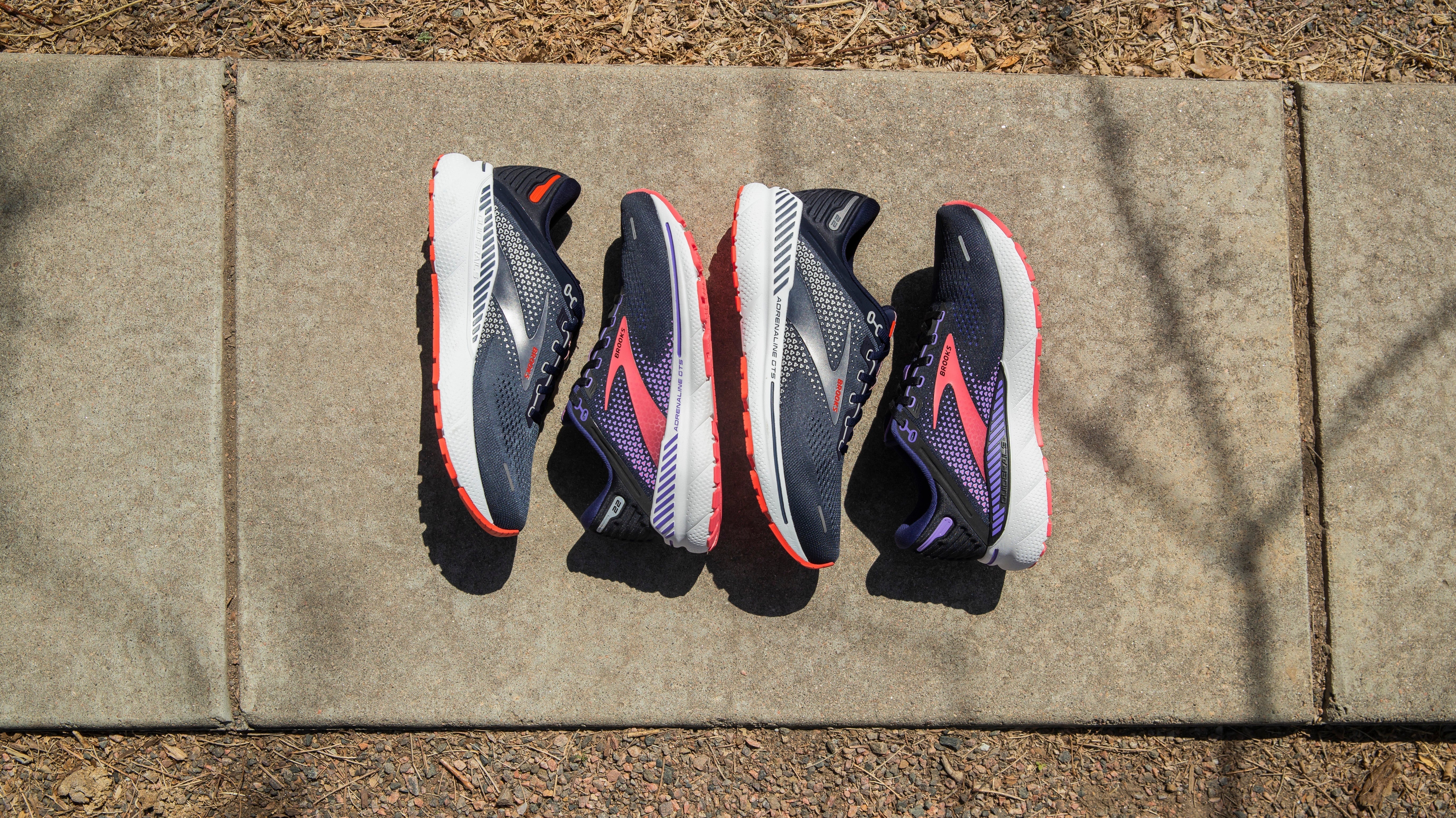 2 Paar BROOKS Adrenaline GTS 22 liegen nebeneinander auf einem Weg.