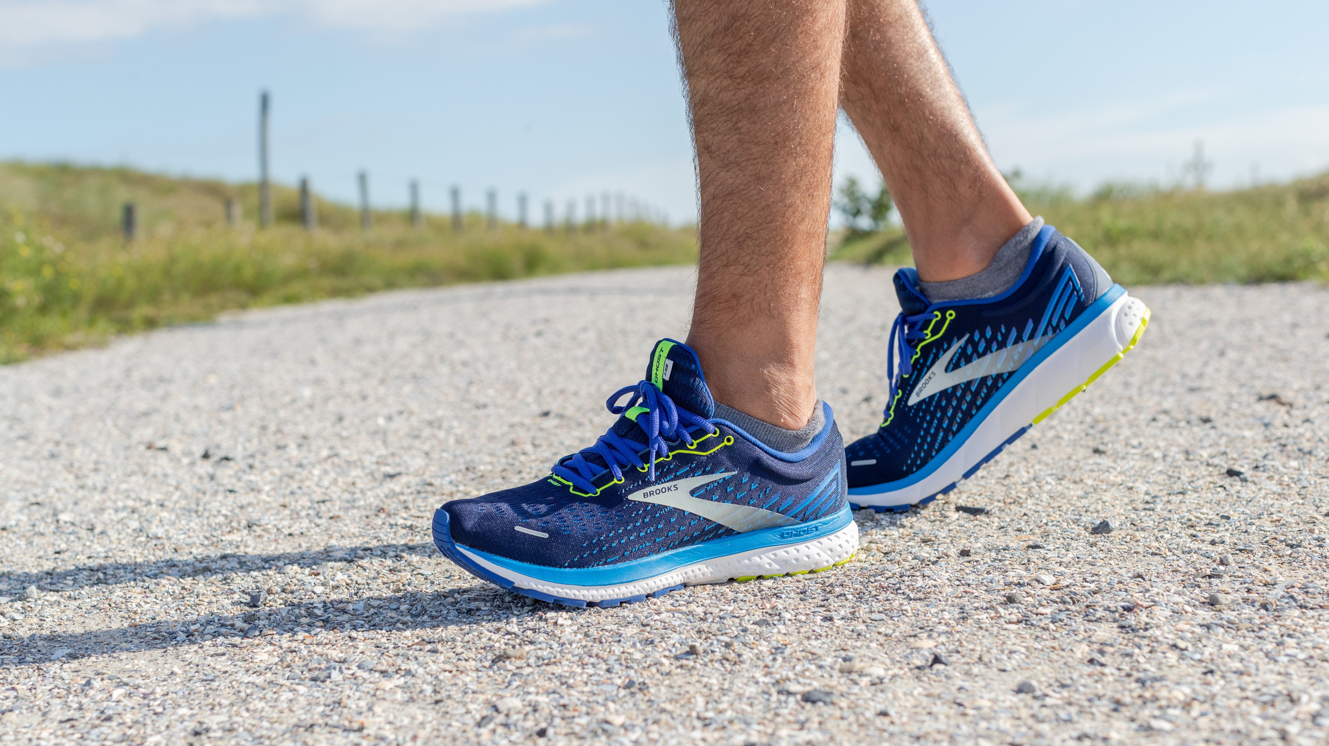 Eine Person steht mit blauen Laufschuhen auf einer Straße. Zu sehen ist nur der untere Teil der Füße mit den Laufschuhen.