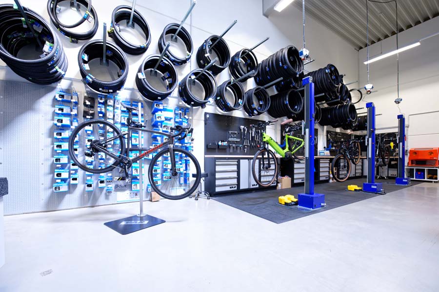 Zu sehen ist die Bike Werkstatt von Sport Kuhn. 3 Fahrräder sind an Hebebühnen aufgebaut. Im Hintergrund befindet sich Werkzeug sowie Fahrrad-Mäntel.