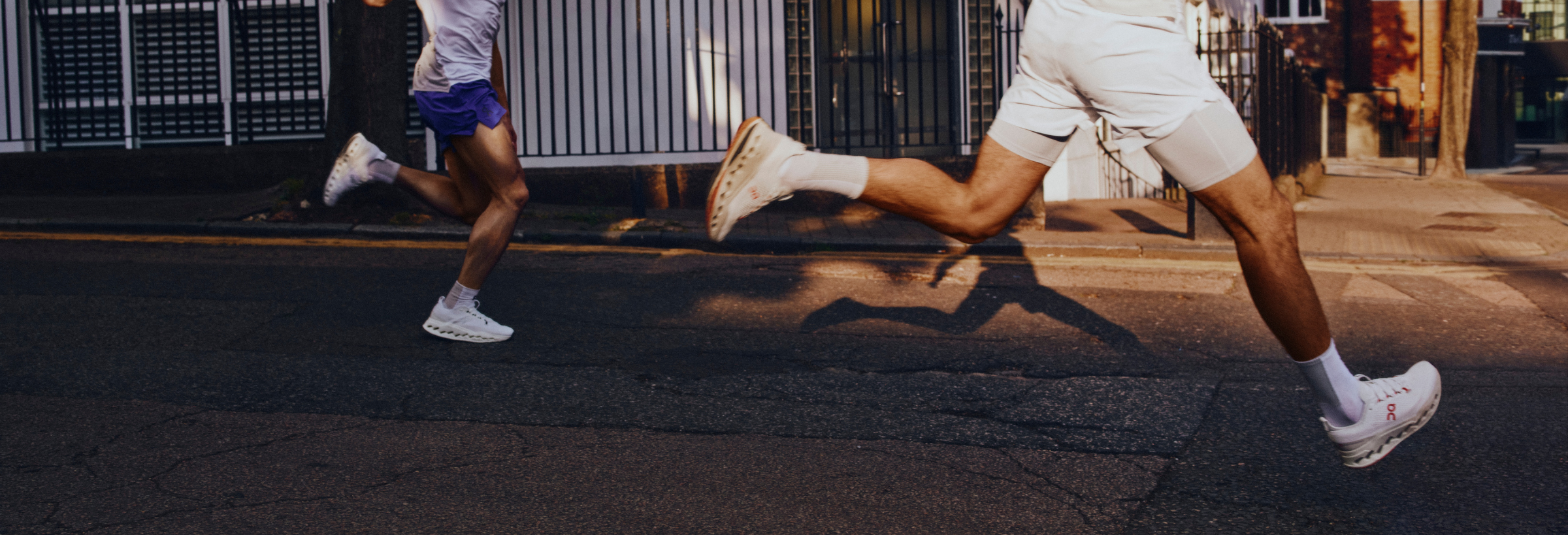 Eine Läuferin und ein Läufer laufen auf der Straße mit Laufbekleidung und Laufschuhen der Marke ON.