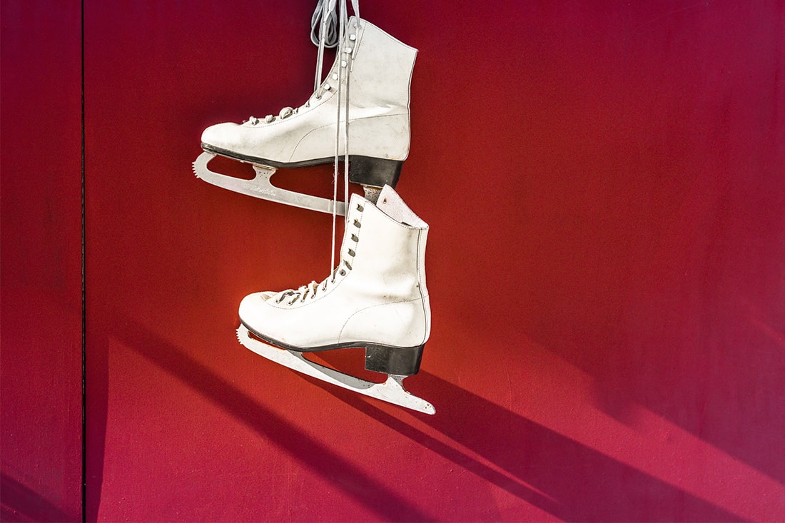 2 aneinander gebundene Schlittschuhe hängen von der Decke. Der Hintergrund ist rot.