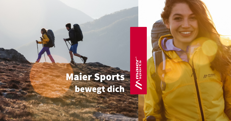 Zwei Personen wandern mit Wanderausrüstung. Rechts im Bild zu sehen ist eine Frau, die eine gelbe Jacke trägt.