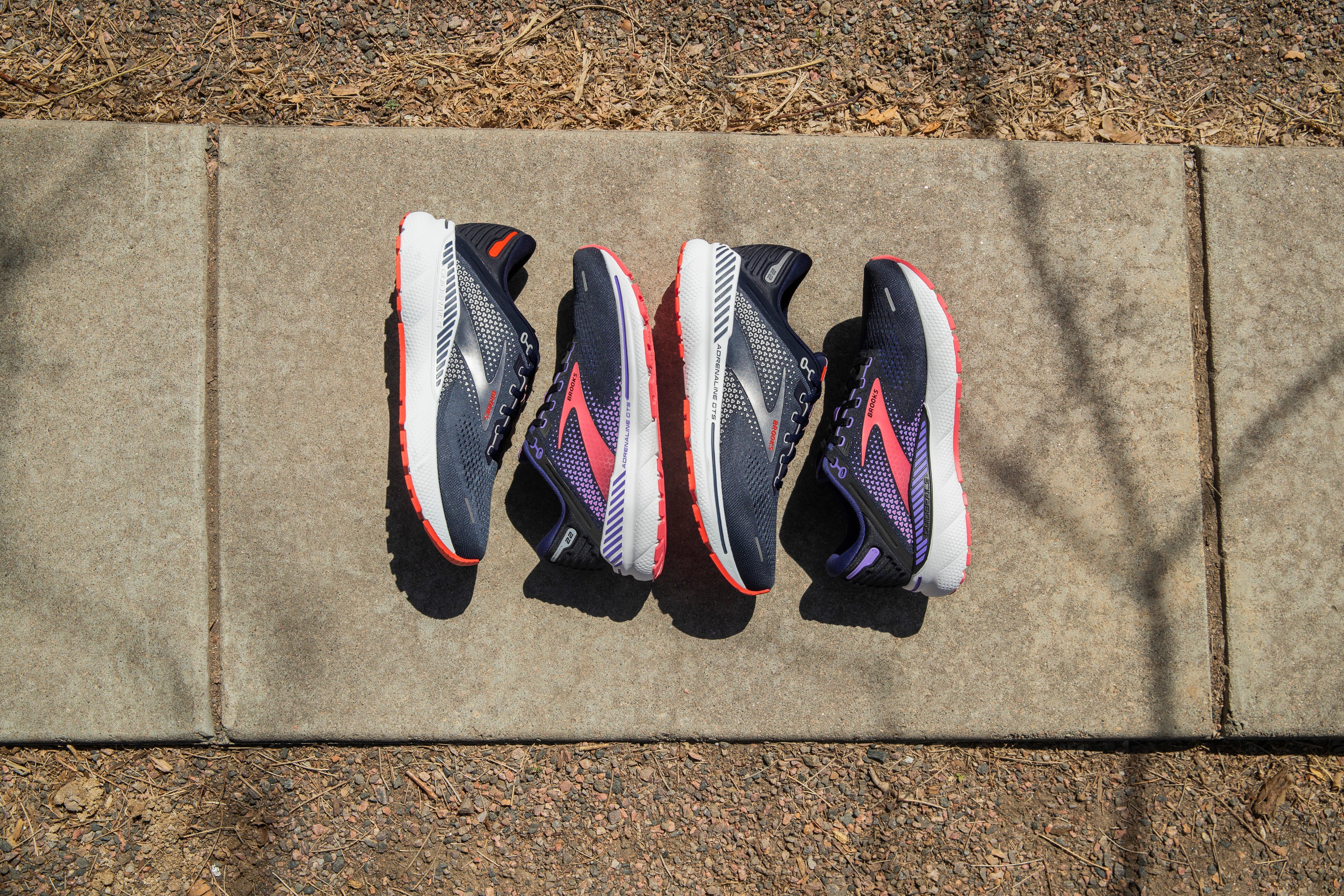 2 Paar BROOKS Adrenaline GTS 22 liegen nebeneinander auf einem Weg.