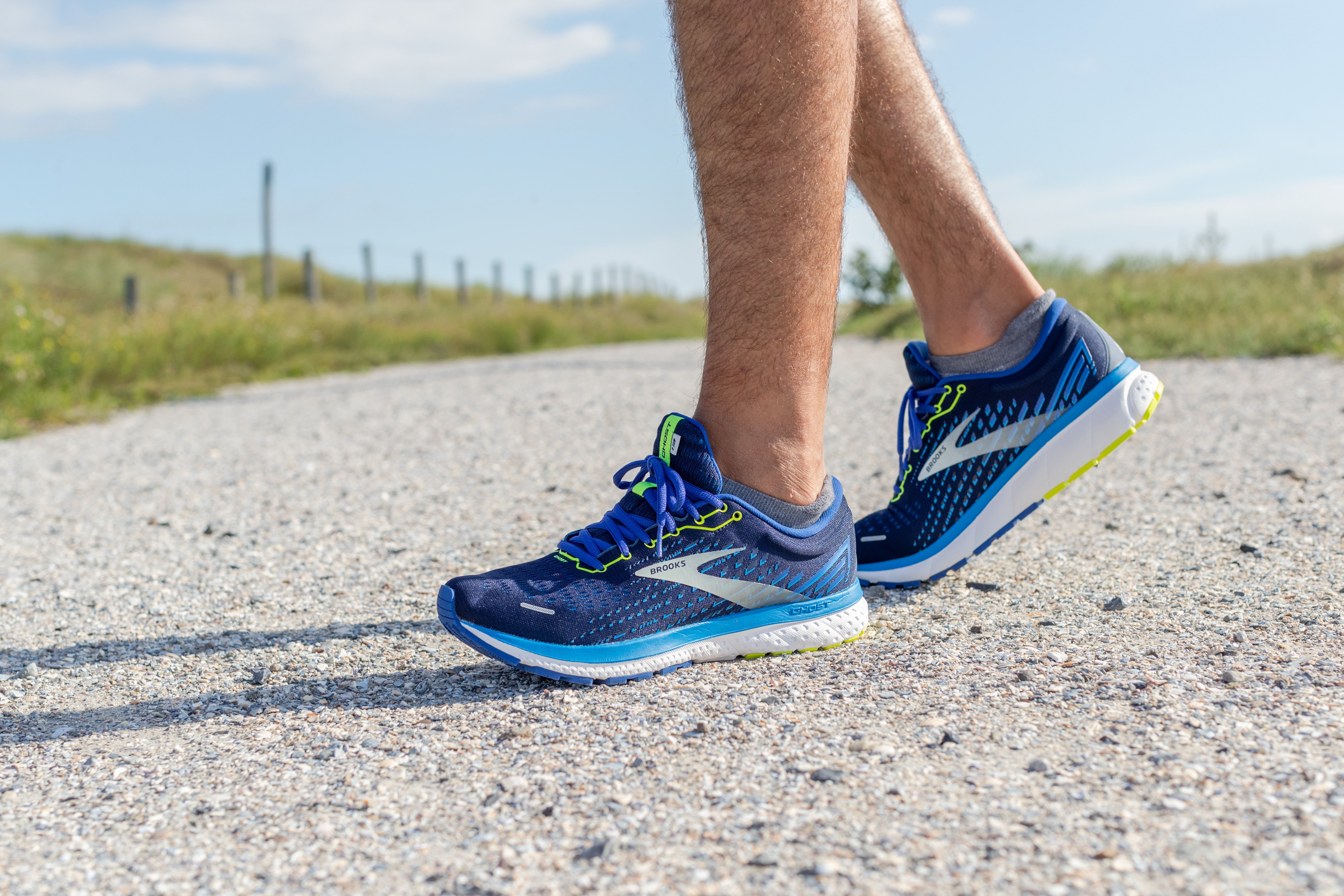 Eine Person steht mit blauen Laufschuhen auf einer Straße. Zu sehen ist nur der untere Teil der Füße mit den Laufschuhen.