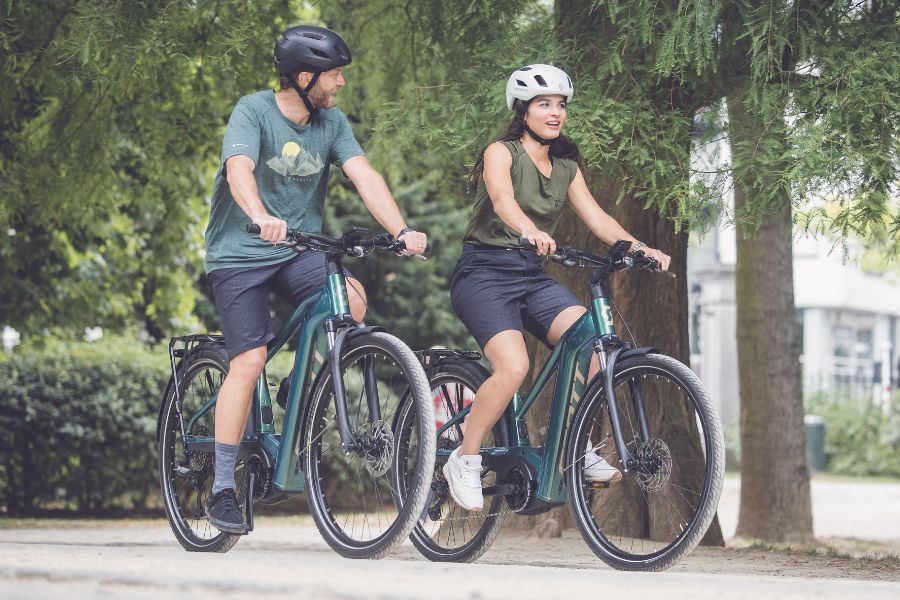 Eine Frau und ein Mann fahren auf SCOTT-E-Bikes durch einen Park.