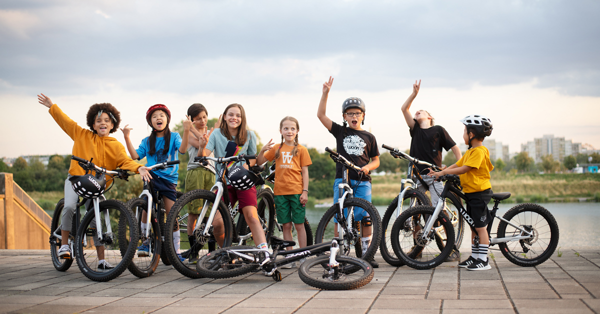 Gruppe von Kindern mit Woom Fahrrädern lächeln und zeigen mit den Händen in die Luft