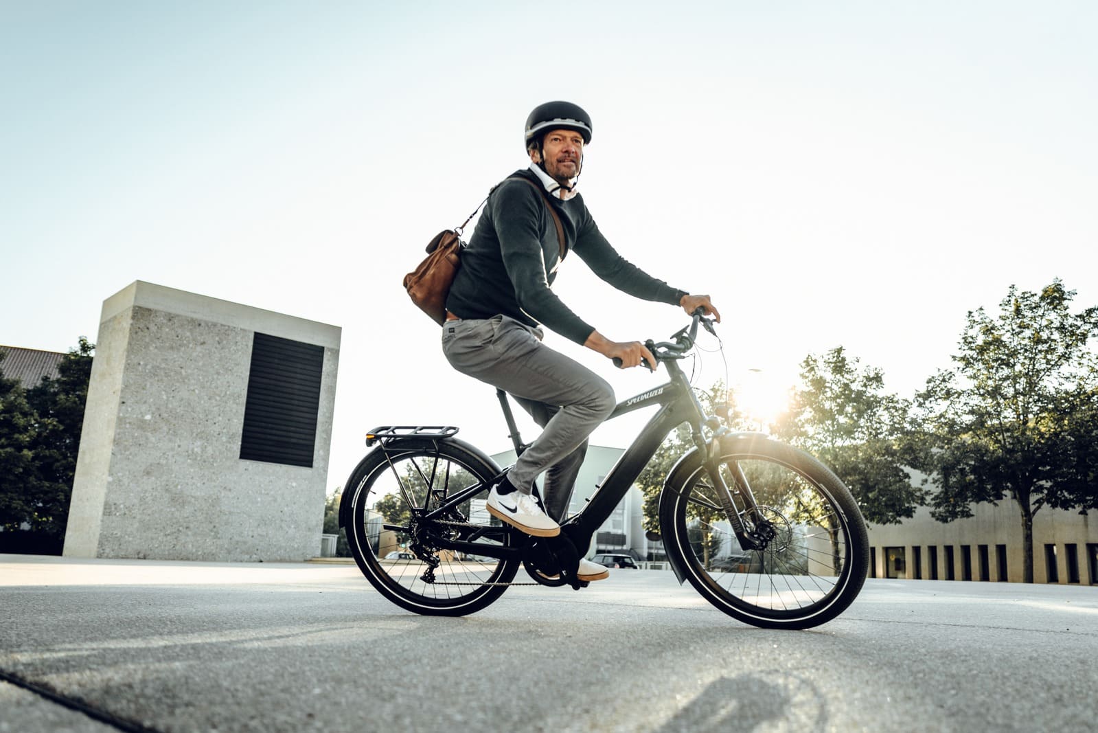 Herr mit Helm und Ledertasche auf einem Specialized Fahrrad dreht eine Kurve auf dem Asphalt.